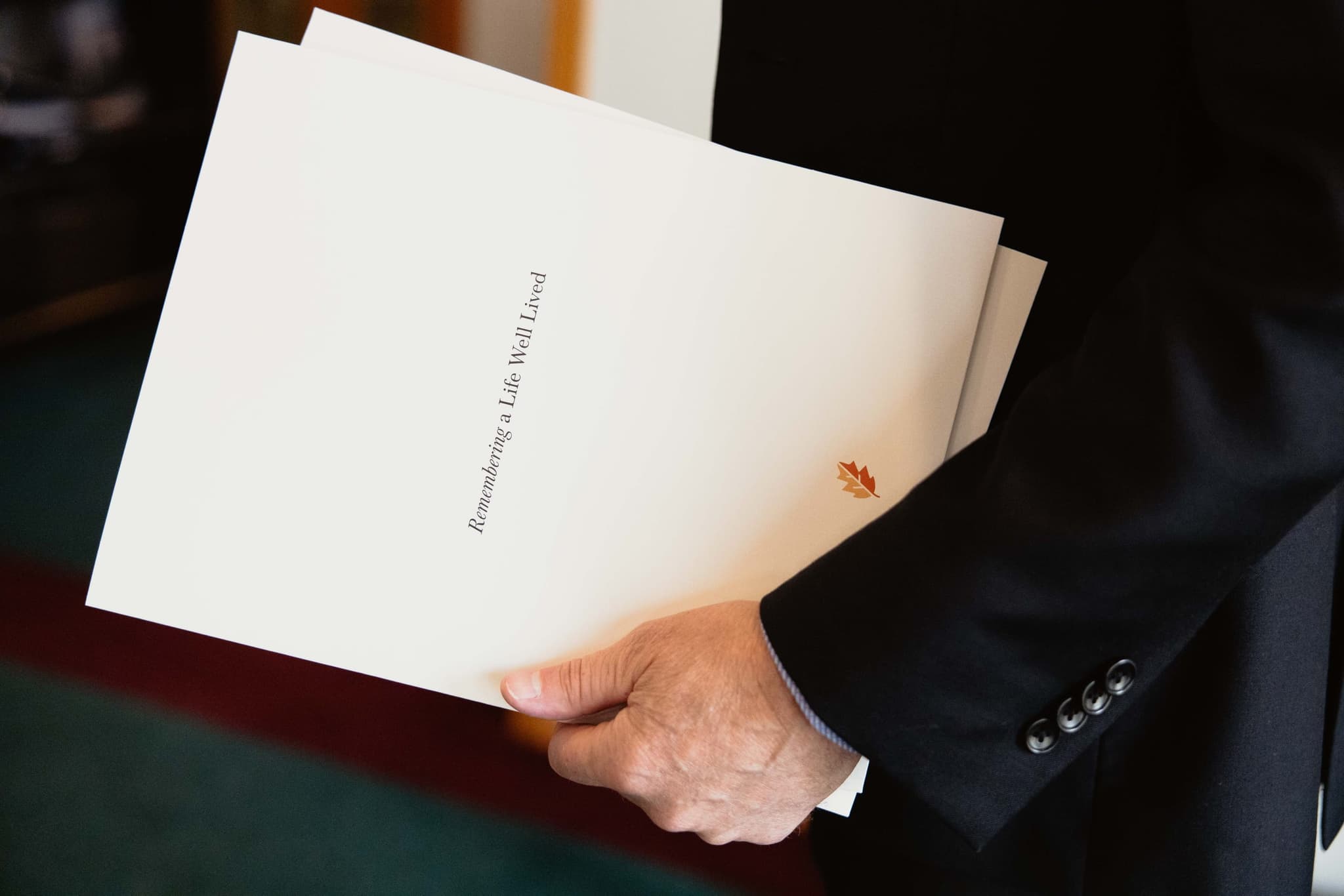 Hands carrying memorial folders with a leaf emblem, reflecting the dignified funeral service of Athabasca Community Chapel