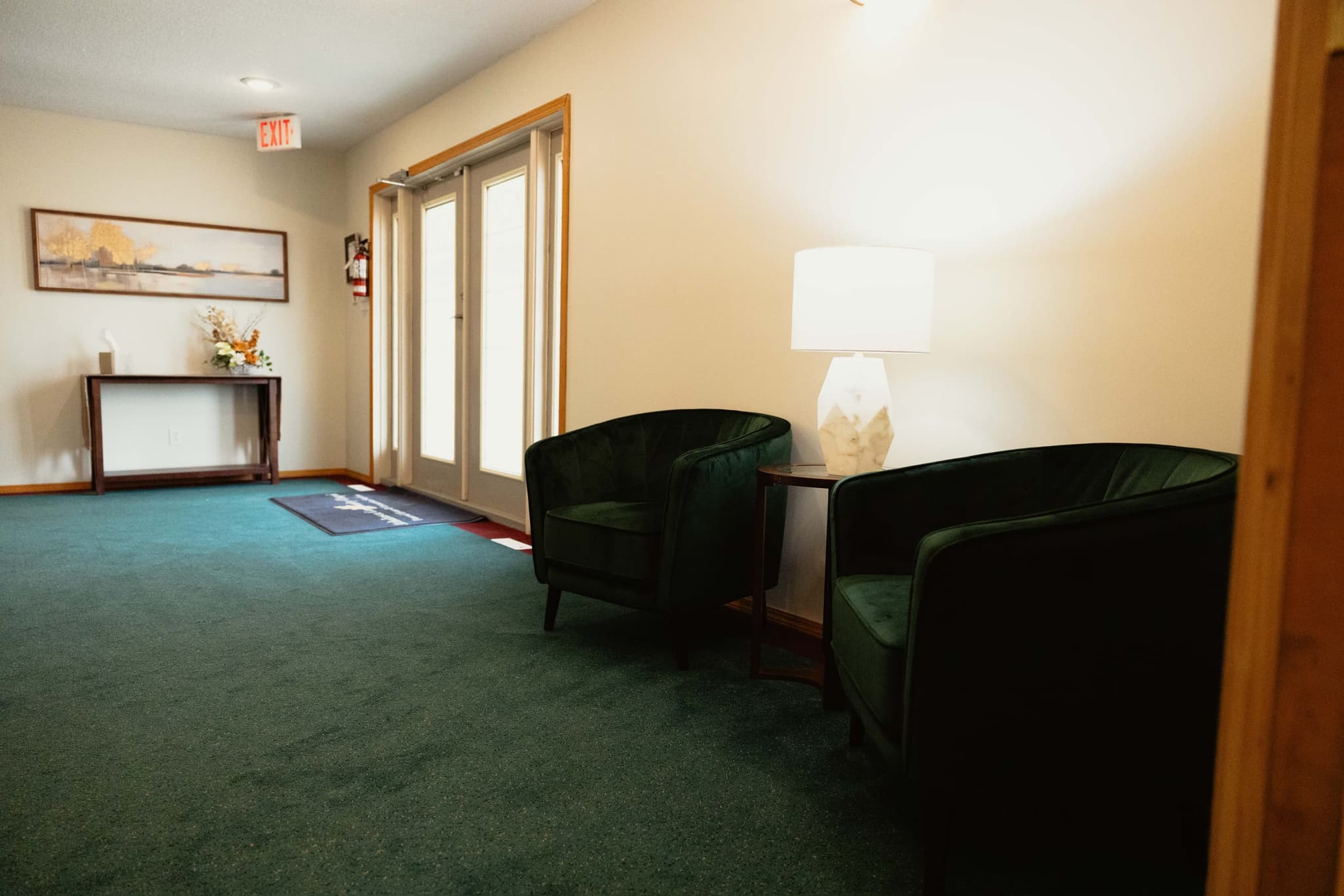 A welcoming lobby corner at Athabasca Community Chapel with green velvet armchairs and a marble lamp, where families receive guidance in Athabasca