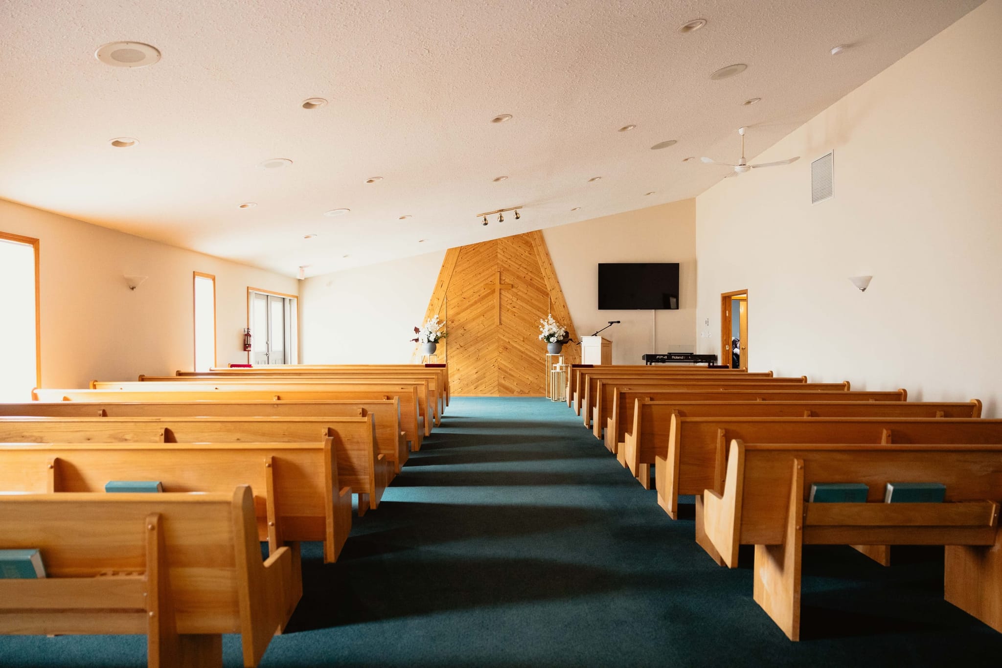 The chapel aisle at Athabasca Community Chapel leading toward the wood altar wall, cross, and white floral arrangements.